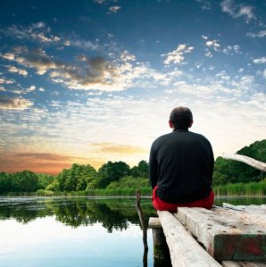Image of man sitting on dock enjoying lake sunrise