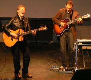 Heather Bishop at the Living Lakes Concert in Winnipeg image of woman singing and playing guitar with man playing guitar in the background